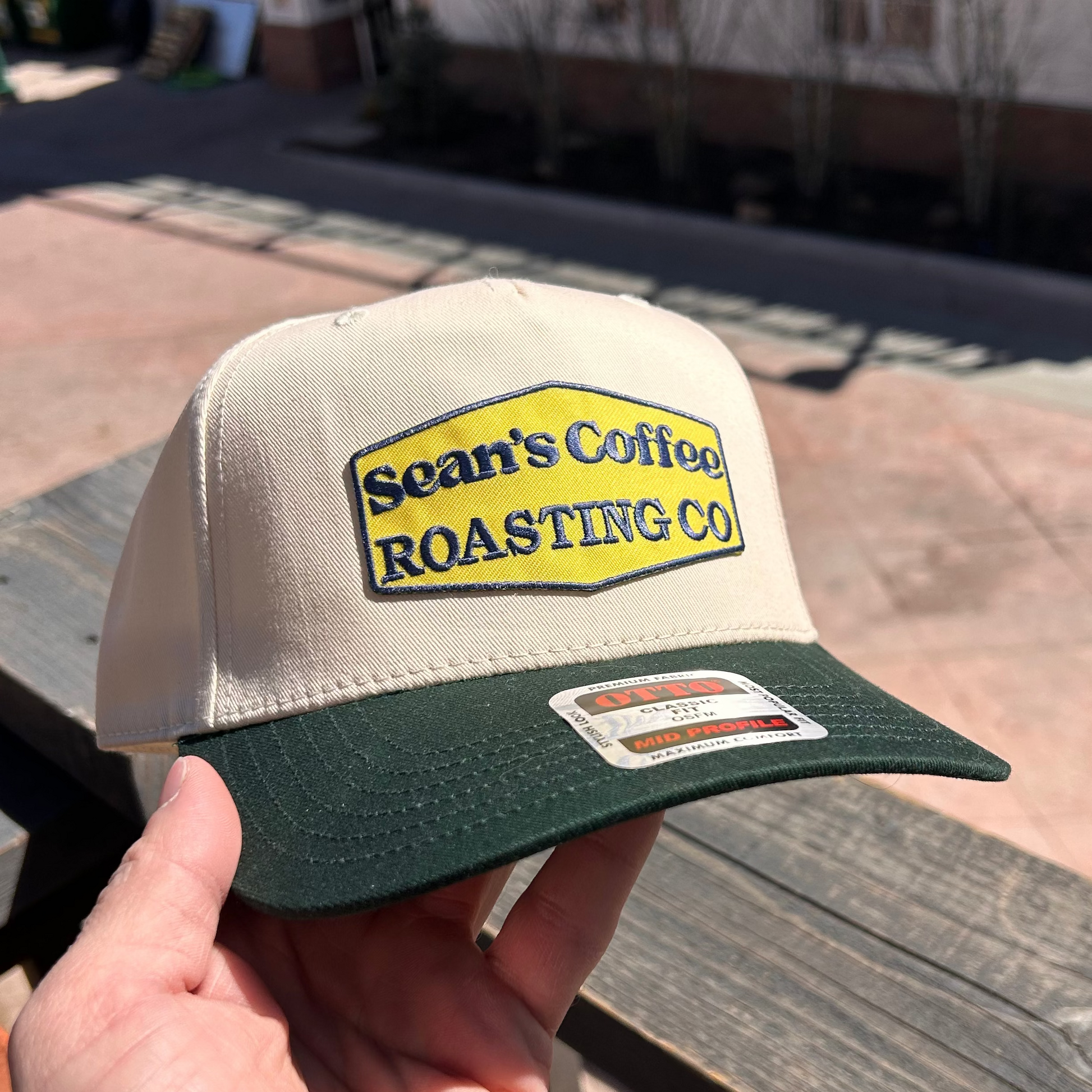 Cap with 'Sean's Coffee Roasting Co' logo held by a hand on a wooden deck.