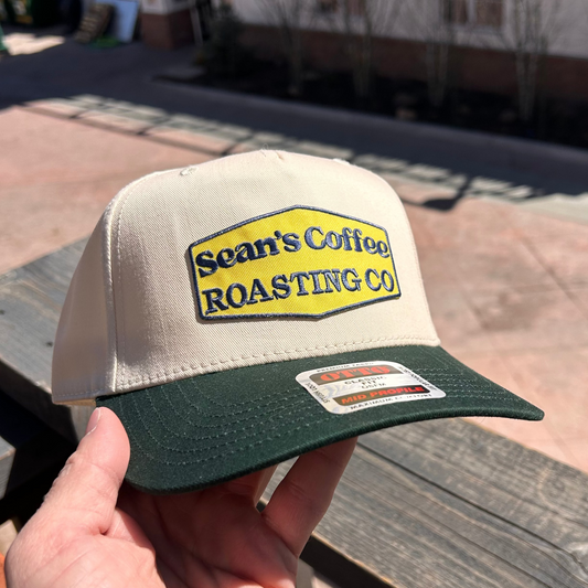 Cap with 'Sean's Coffee Roasting Co' logo held by a hand on a wooden deck.